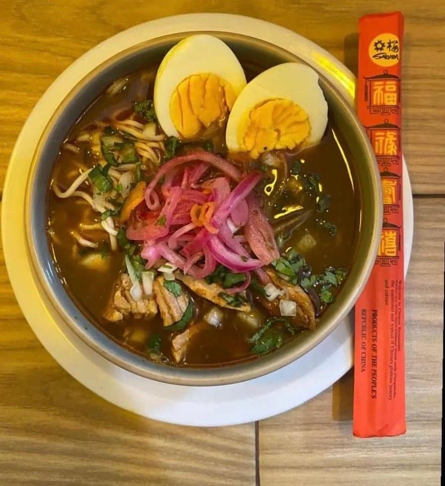 Plato de birriamen con huevo cocido, cebolla morada y cilantro