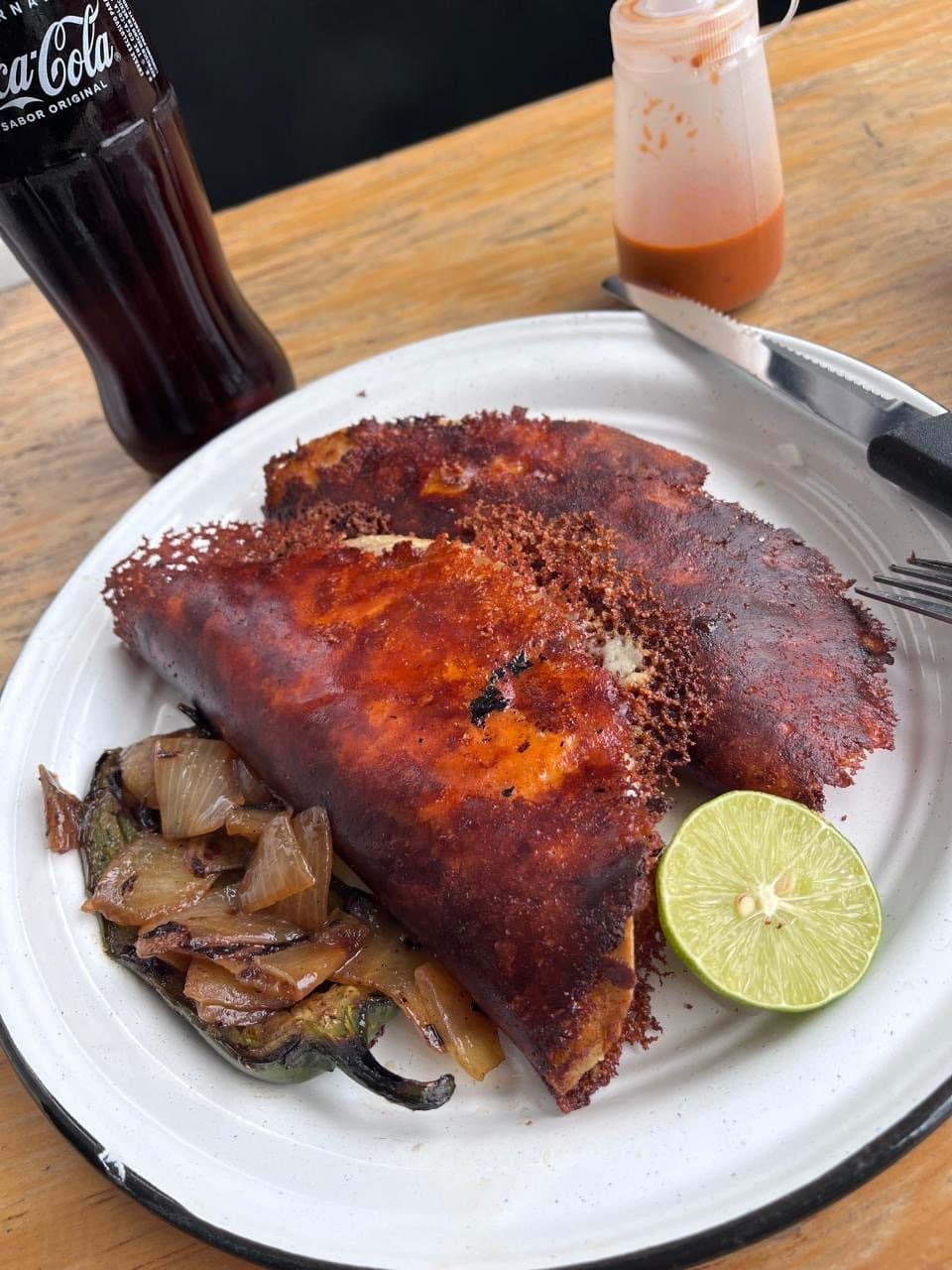 Dos quesabirrias invertidas con el queso tostado por fuera, cebollas y chiles toreados y limón en plato blanco