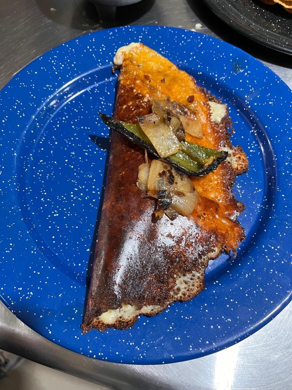 Taco low de birria con costra de queso dorado, chile y cebolla toreados sobre plato de peltre azul